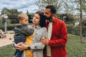 Young family spending time together outdoors in a park. Mother holds a toddler while father...