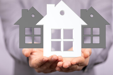 Image of a real estate agent's hands holding three house models, symbolizing home ownership and...