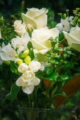 Close up of a lush bouquet of fresh white roses and delicate blooms arranged in a glass vase, set...