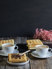 Rustic breakfast setup with coffee and waffles topped with chocolate spread, served on a wooden table in a cozy, home-style atmosphere.
