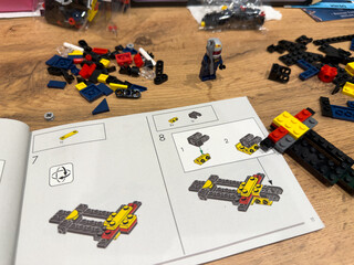 Obraz premium Moscow, Russia, April 26, 2025: LEGO Speed Champions Formula 1 Red Bull Racing car assembly in progress. Step by step building instructions, colorful bricks and driver mini figure on wooden table