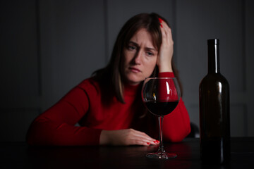 Alcohol addiction. Woman at wooden table indoors, focus on glass of red wine and bottle