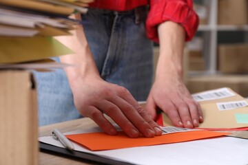 Woman putting barcodes onto envelopes at table in post office, closeup