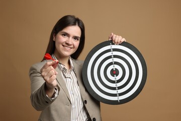 Targeting. Smiling businesswoman with dart board and arrow on beige background