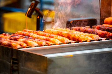 a sausage is being lifted by tongs and placed on a red-hot grill,