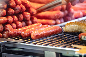 a sausage is being lifted by tongs and placed on a red-hot grill,