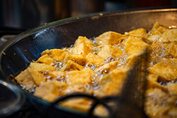  pieces of tofu are being deep-fried in a hot oil wok until golden and crispy