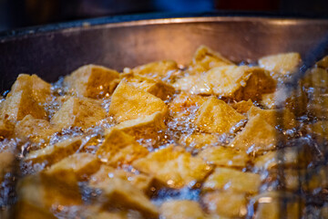  pieces of tofu are being deep-fried in a hot oil wok until golden and crispy