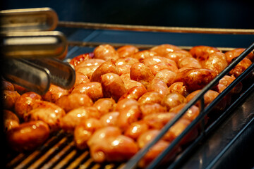 a close-up view of mini sausages being grilled over an open flame at a night market. 