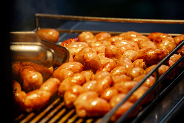 a close-up view of mini sausages being grilled over an open flame at a night market. 