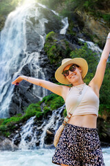 Portrait young adult happy smile woman wear hat sunglasses enjoy hiking Haslach village Staniskabach Schleierfall waterfall Tyrol Austria Austrian Alps. Female person joyful journey. Summer vacation