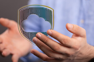 Image of hands holding a digital shield protecting a cloud, symbolizing secure cloud computing and...