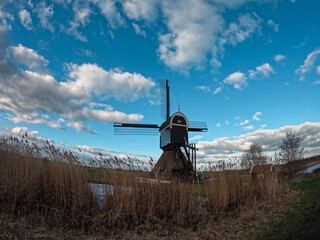 An ancient Dutch windmill used for pumping water on a blue sky with white clouds. Amazing landscape from the Netherlands at dusk in spring time 