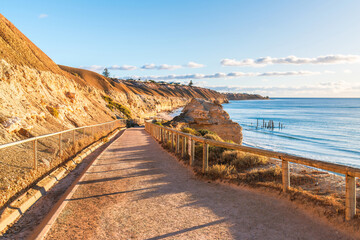 Walking trail to Port Willunga beach, while old jetty ruins can be seen in the sea at sunset time, Fleurieu Peninsula, South Australia