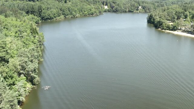 Aerial view high above tranquil lake winding through dense green forest landscape, Marcillac La Croisille, France