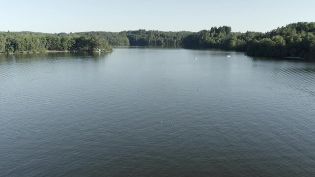 Aerial view flying over historic metal truss Pont de Lantourne bridge spanning wide lake, forested shores, Marcillac La Croisille, France