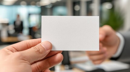 Hand holds blank business card in office setting with blurred background.