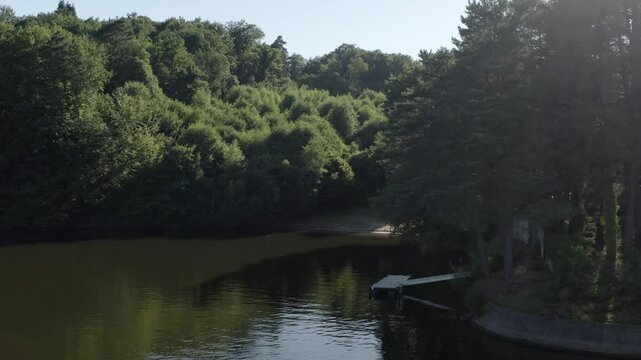 Aerial view of secluded wooden dock on calm lake surrounded by dense green forest, Marcillac La Croisille, France
