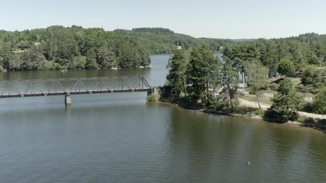 Aerial view rising over calm lake, revealing Pont de Lantourne bridge and forested shoreline, Marcillac La Croisille, France
