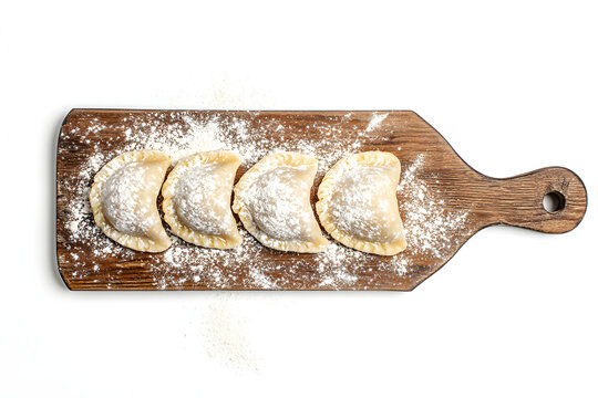 Large fresh dumplings on a wooden cutting board with a white background.