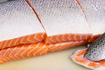 Fresh raw salmon fillets with skin neatly sliced and arranged on a cutting board. The rich orange...