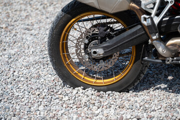Obraz premium Close-up view of motorcycle wheel on gravel surface during sunny outdoor setting