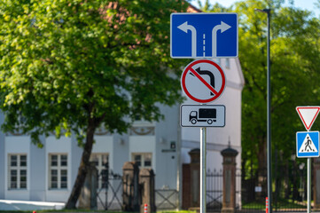 Fototapeta premium Traffic signs direct vehicles at a junction while nearby a historic building stands.