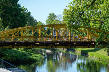 Obraz premium Colorful bridge spanning a calm river surrounded by lush greenery on a sunny day