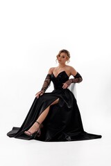 Elegant young woman in black evening gown poses gracefully against a white background during a...