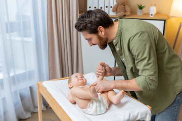 Dad changing a diaper to his little baby boy while the kid smiling and looking happy