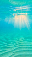 Textured sand sea floor and sun rays penetrate the water.