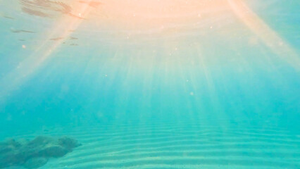 Textured sand sea floor and sun rays penetrate the water.