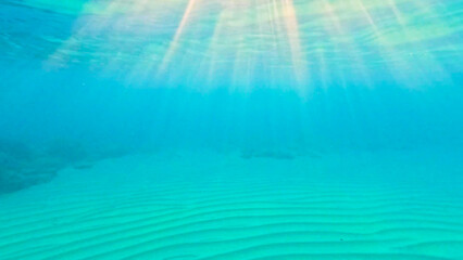 Textured sand sea floor and sun rays penetrate the water.