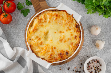 Potato gratin with cream, cheese and garlic in a white ceramic form on a gray concrete background. Potato casserole. Top view, copy space.