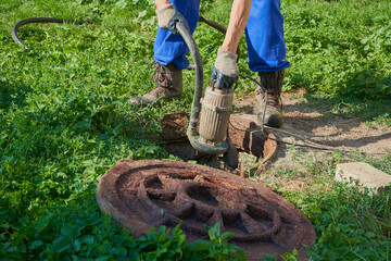 Immersion of the drainage pump in a cesspool, a man holds a hose with a vacuum pump and immerses it...
