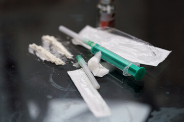 Syringes filled with liquids and powdered substances are placed on a reflective surface. The...