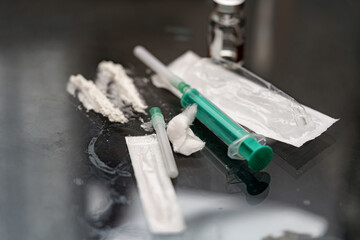 Syringes filled with liquids and powdered substances are placed on a reflective surface. The...