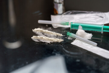 Syringes filled with liquids and powdered substances are placed on a reflective surface. The...