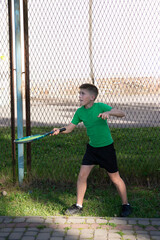 Young boy practices his tennis serve near a chain-link fence.