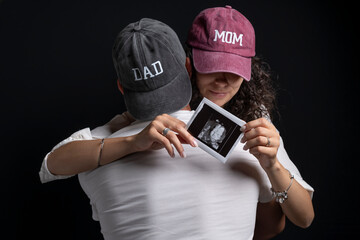 A pregnant woman is hugged by a man while holding the ultrasound results of her unborn baby