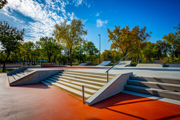 Concrete skatepark with stairs and handrails, surrounded by plants in the background, perfect for street skating and tricks.