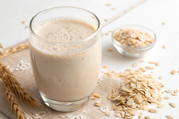 Creamy oat smoothie in glass with oats scattered on table.