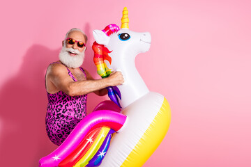 Elderly man in leopard print swimsuit having fun with unicorn float against pink background © deagreez