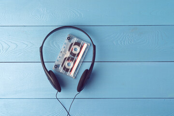 Transparent cassette and headphones evoke iconic '90s memories, placed on a bright blue wooden...