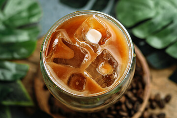 Top view of iced coffee with milk and melting ice, green leaves and coffee beans nearby add freshness and a cozy, inviting mood.