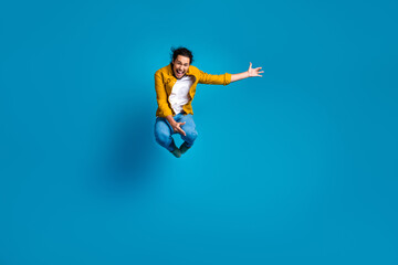 Fototapeta premium Cheerful young man jumping with excitement wearing stylish outfit against bright blue background conveying joy and energy