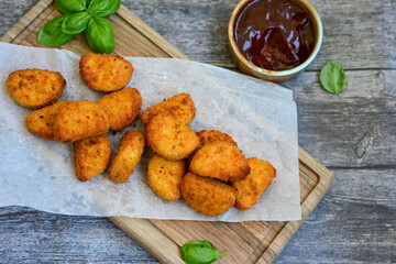 
 Crispy oven baked  chicken nuggets and  barbeque sauce . Breaded chicken fillets  with chilly peppers and fresh basi on wooden rustic background
