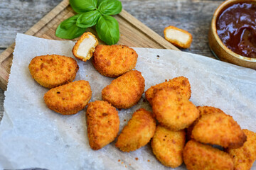 
 Crispy oven baked  chicken nuggets and  barbeque sauce . Breaded chicken fillets  with chilly peppers and fresh basi on wooden rustic background
