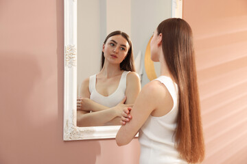 Beautiful woman looking at herself in mirror indoors