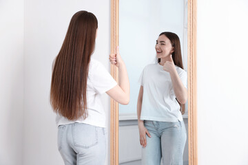 Beautiful woman showing thumbs up near mirror indoors